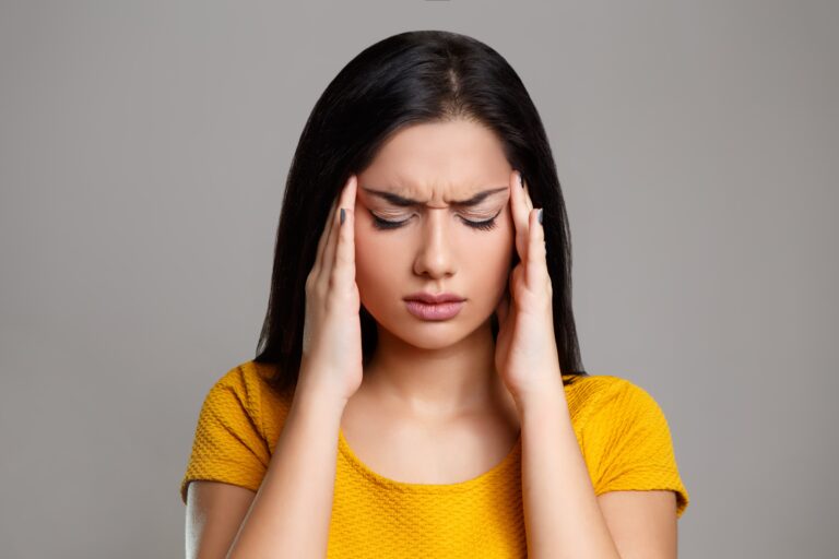 woman in yellow shirt holding her temples in pain