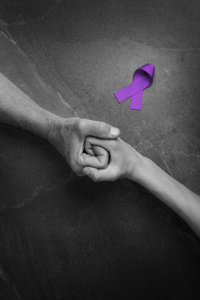 Two hands holding one another with a purple ribbon in the background