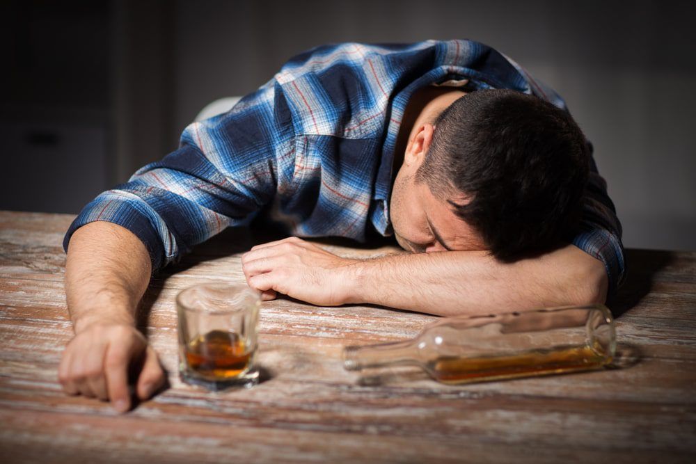 man face down on table with bottle and drink in front of him
