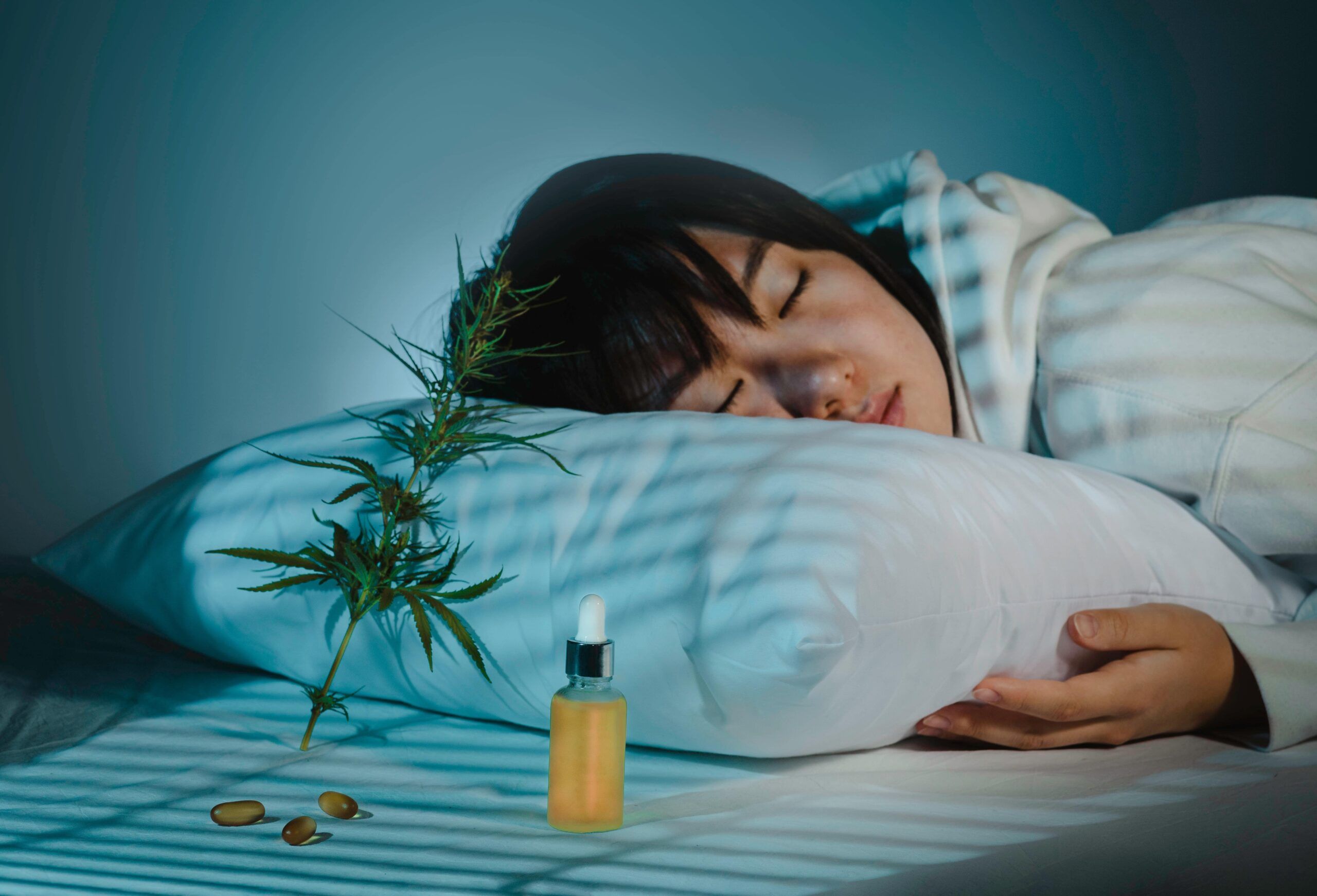 Asian girl sleeping in evening bedroom with cbd oil, capsules and a cannabis branch. Melatonin production, concept of combat sleep disorders