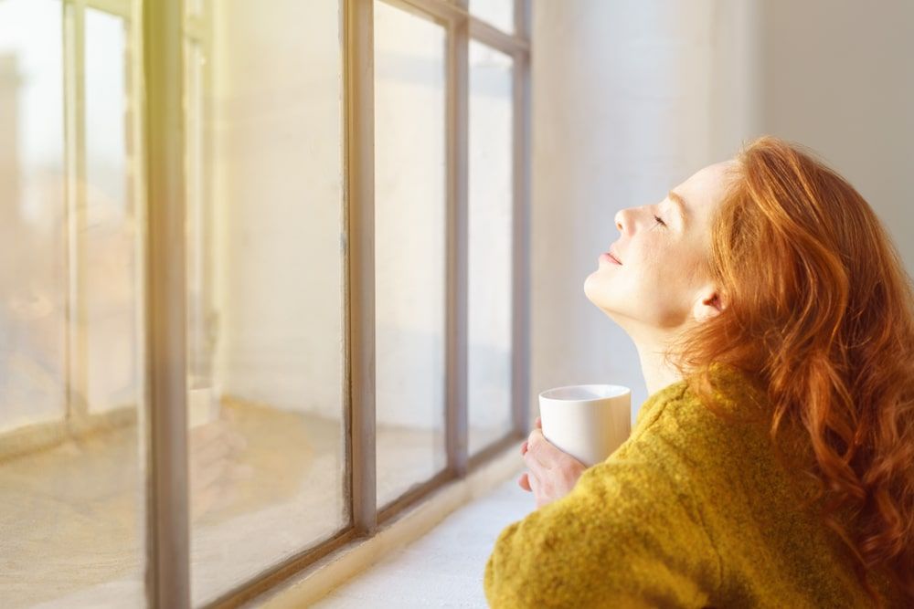 woman smiling looking out the window with sunlight streaming through